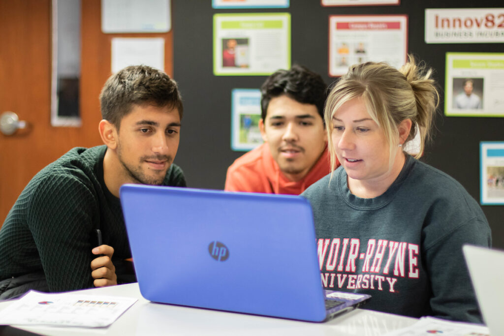 Three students working on assignment on laptop during class