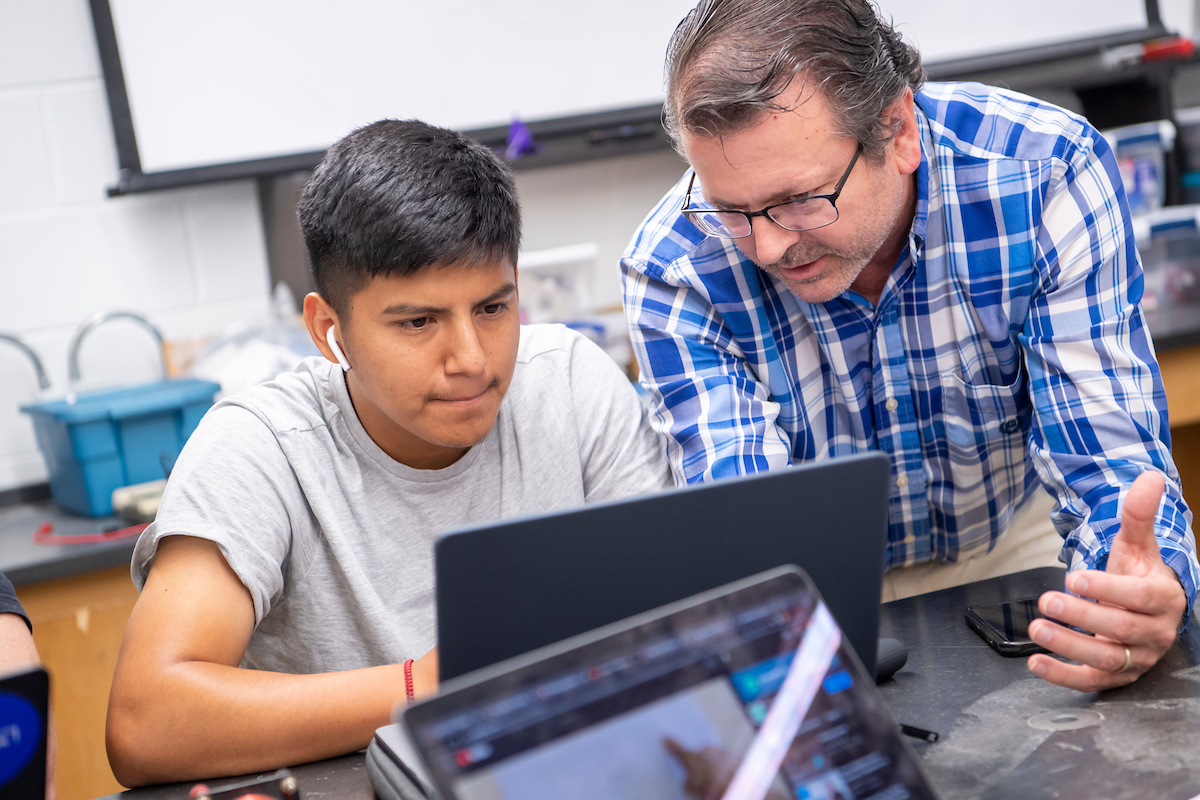 Professor helps student on laptop during a physics lab