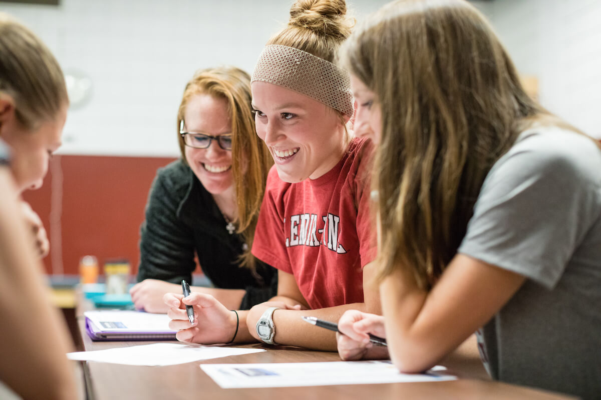 Three smiling students participate in table top assignment during class